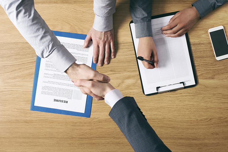 handshake during interview with resume and contract agreement on table