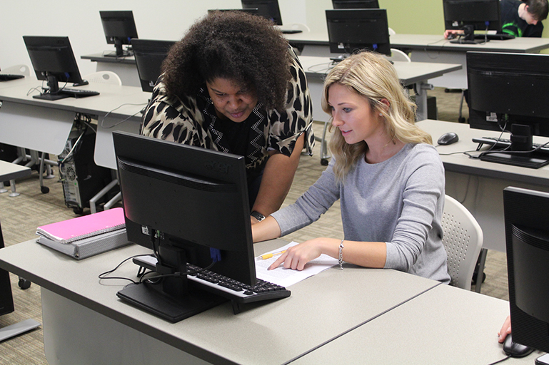 A woman instructor assisting a student in a computer lab