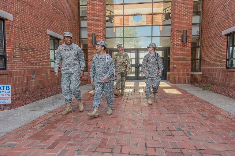 Four ROTC students chatting together while walking out of a brick building