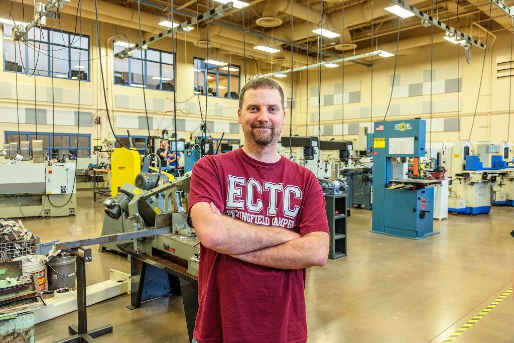 guy in ectc shirt standing with arms crossed in shop