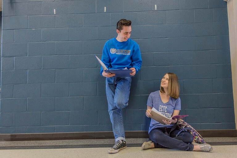male student leaning against a wall and a female student sitting on the floor