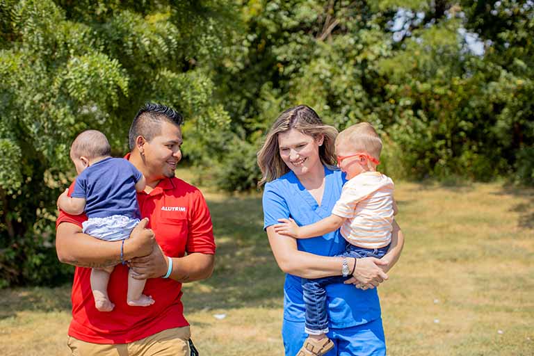 two people, each holding a toddler in their arms and one wearing scrubs