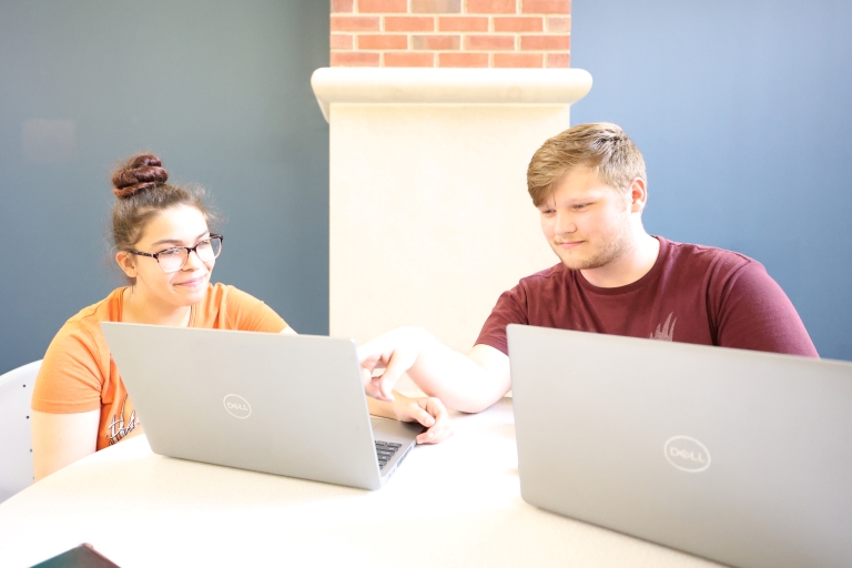 two students working on laptops at a desk
